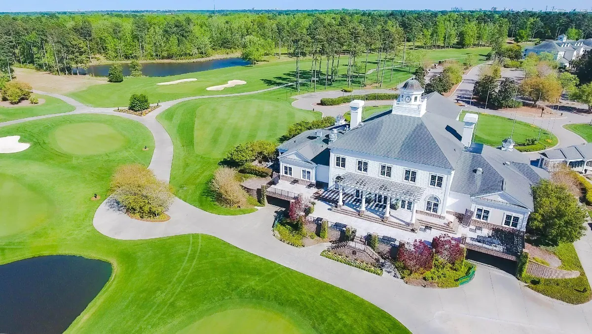 This exterior shot shows the grand clubhouse overlooking the lush golf course, with water features and mature trees dotting the landscape. The clubhouse’s outdoor patio offers views of golfers and social gatherings, enhancing the luxurious resort vibe.