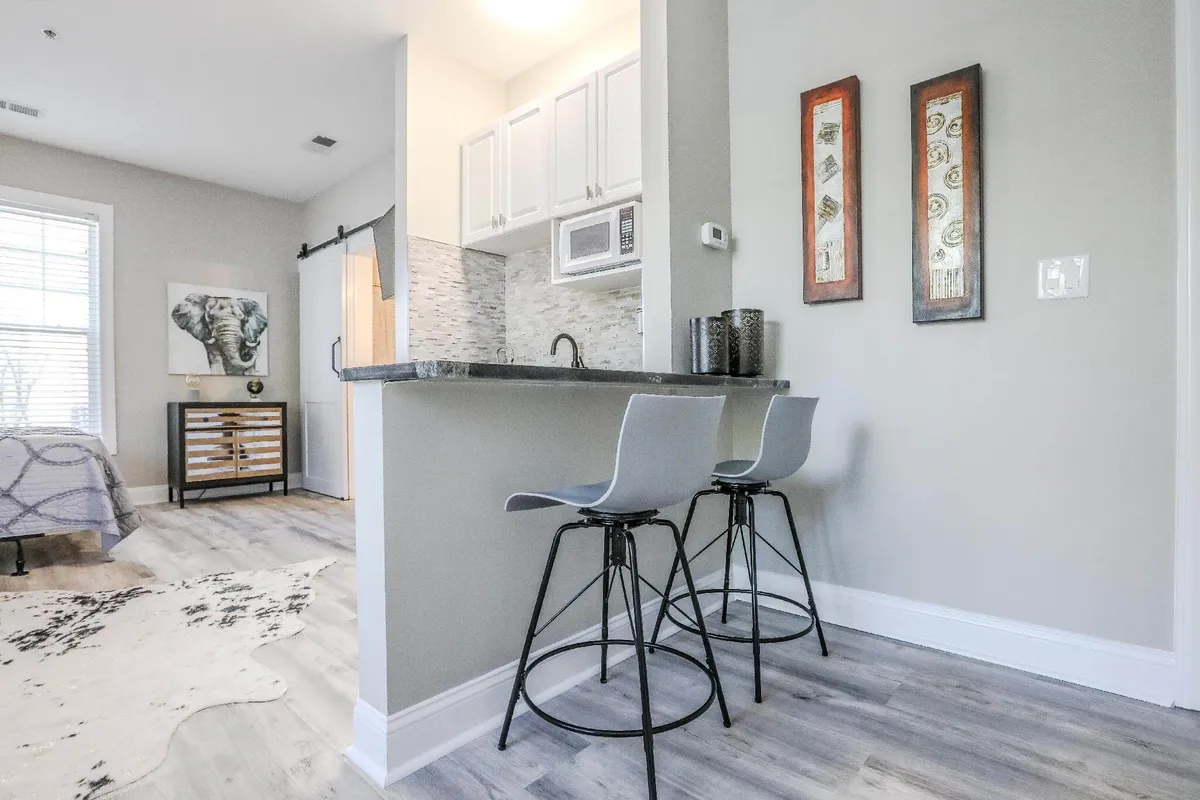 A stylish kitchen area with a counter, bar stools, a striking elephant artwork, and a textured rug. The setup encourages casual dining or morning coffee, with a modern and welcoming atmosphere.
