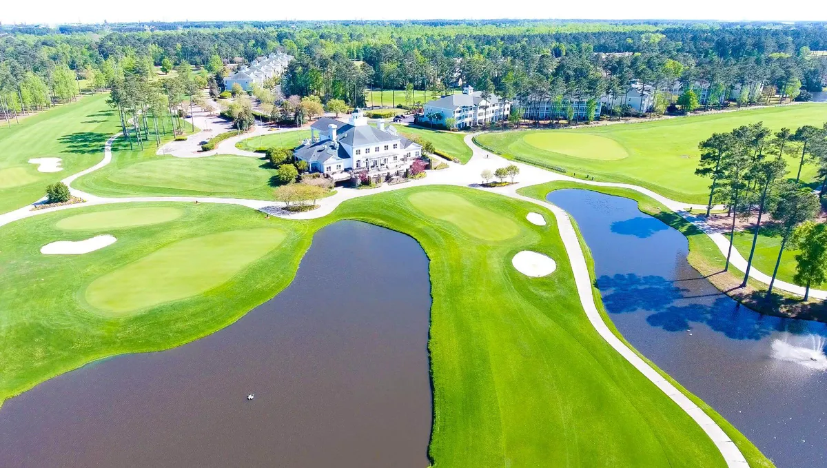 An expansive view of the World Tour Golf Course, featuring lush green fairways, the elegant clubhouse in the background, serene water features, and carefully maintained landscaping. Several golfers can be seen enjoying a round, while others relax by the water’s edge.